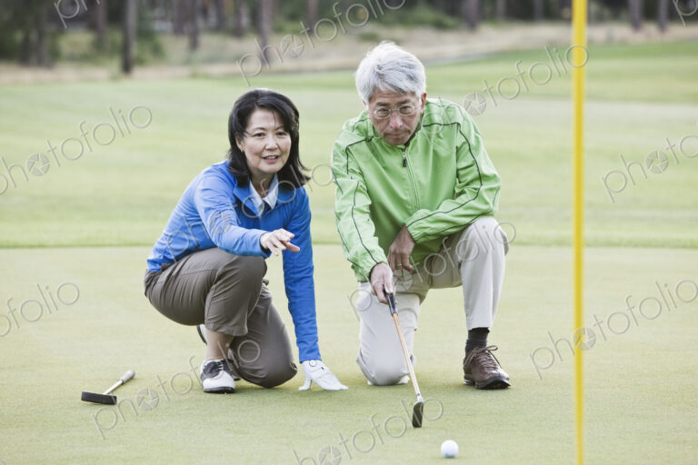 Asian senior couple taking a look at the direction of the next putt on the green.