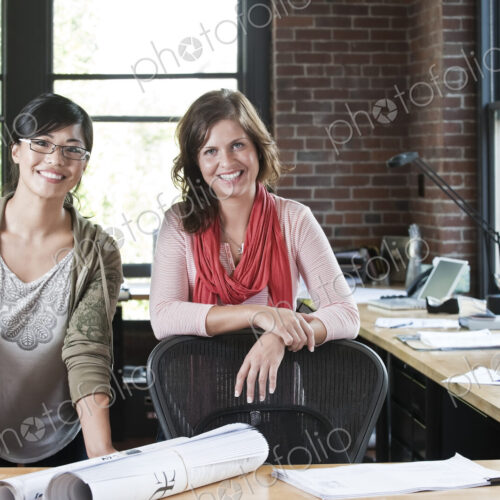 Asian woman and Caucasian woman at a workstation in a creative office.