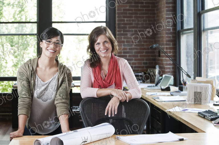 Asian woman and Caucasian woman at a workstation in a creative office.