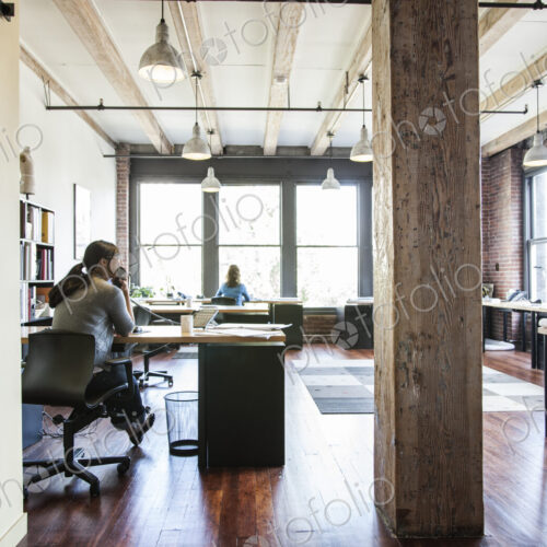 Asian woman and HIspanic man working at their desks in a creative office. Asian woman and HIspanic man working at their desks in a creative office.