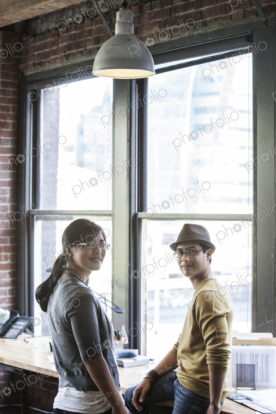 Asian woman and Hispanic man together next to large windows in a creative office.