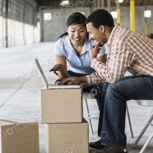 Asian woman and black man using boxes as desk and working on lap top computer in front… Asian woman and black man using boxes as desk and working on lap top computer in front…