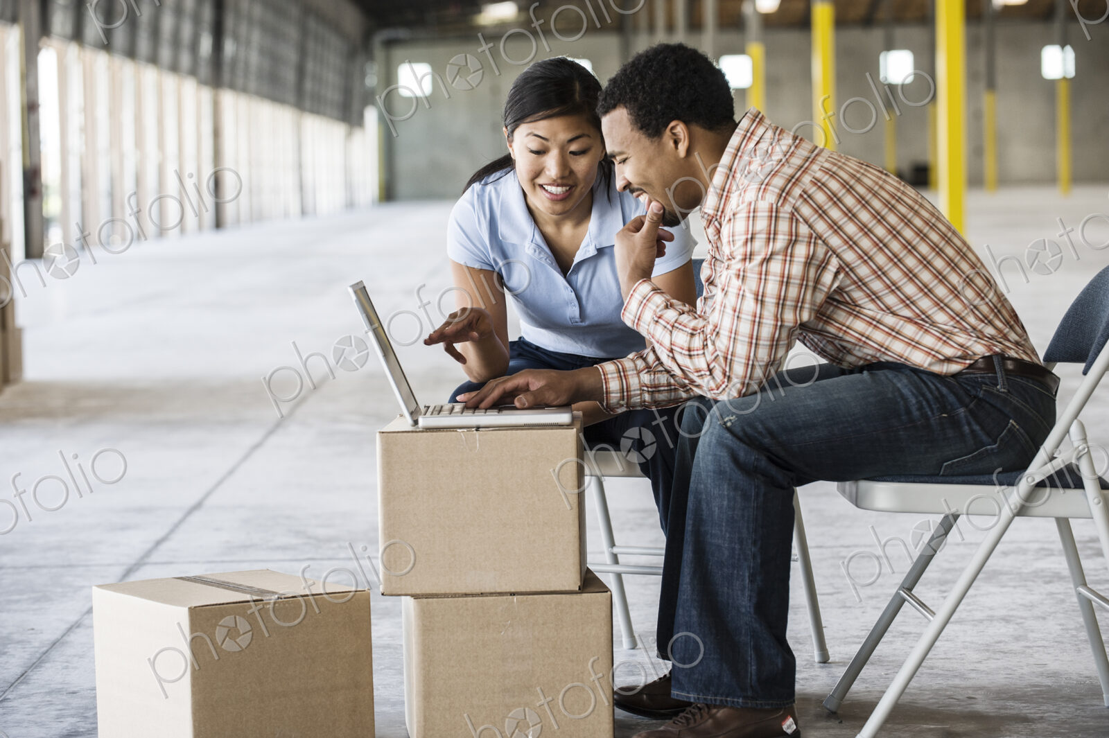Asian woman and black man using boxes as desk and working on lap top computer in front…