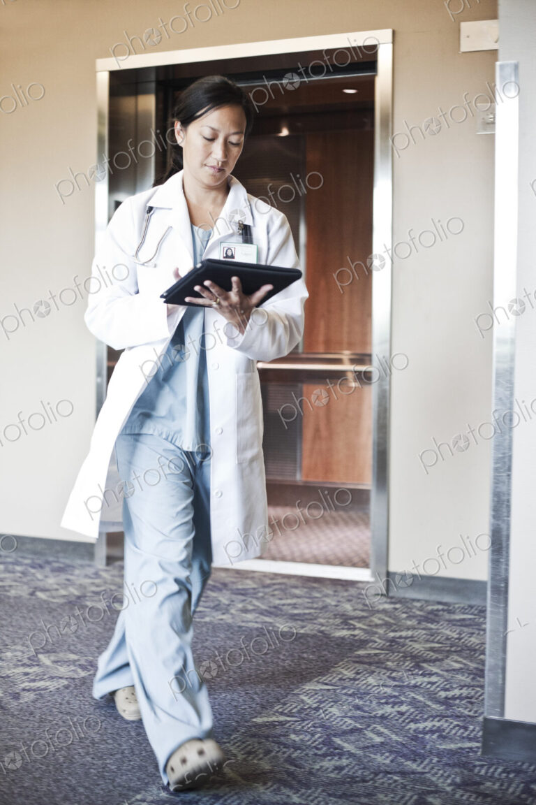 Asian woman doctor walking in a hospital hallway while working on a notebook computer.