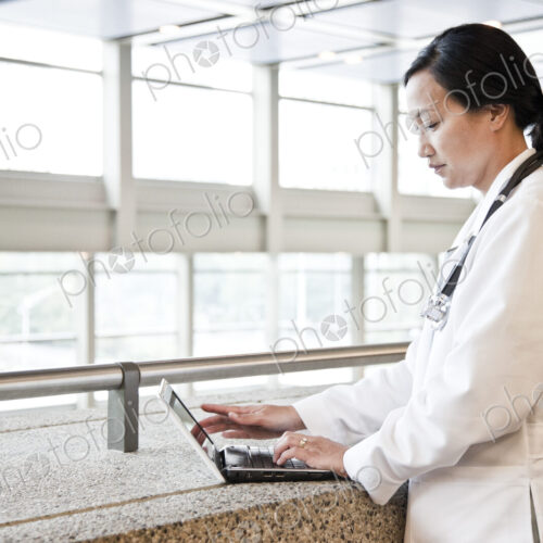 Asian woman doctor working on a lap top in a hospital hallway. Asian woman doctor working on a lap top in a hospital hallway.