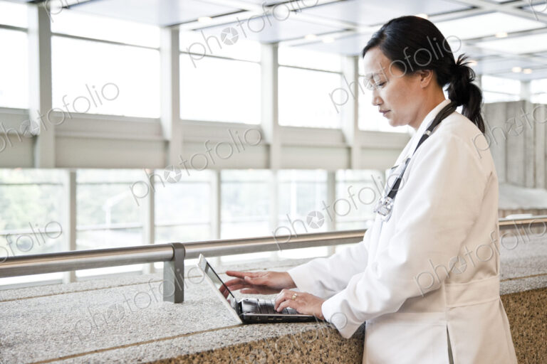 Asian woman doctor working on a lap top in a hospital hallway.