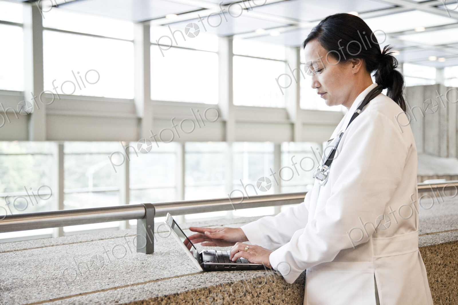Asian woman doctor working on a lap top in a hospital hallway.