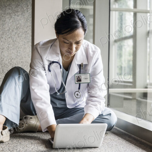 Asian woman doctor working on a lap top in a hospital hallway. Asian woman doctor working on a lap top in a hospital hallway.