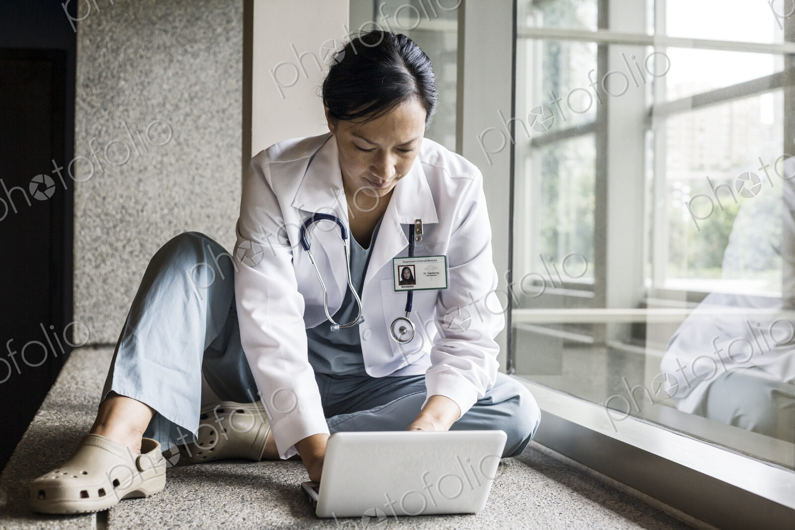 Asian woman doctor working on a lap top in a hospital hallway.