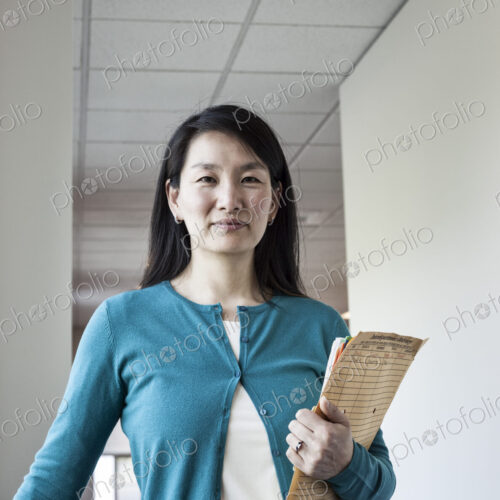 Asian woman holding paperwork in an office hallway. Asian woman holding paperwork in an office hallway.