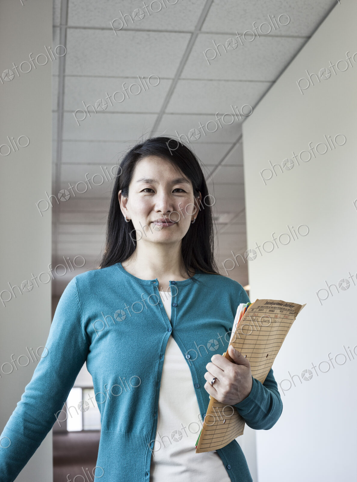 Asian woman holding paperwork in an office hallway.
