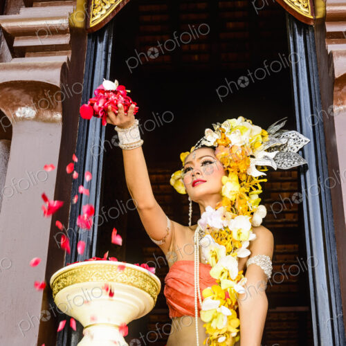 Asian woman scattering flowers from ornate temple window, Chiang Mai, Chiang Mai, Thailand Asian woman scattering flowers from ornate temple window, Chiang Mai, Chiang Mai, Thailand