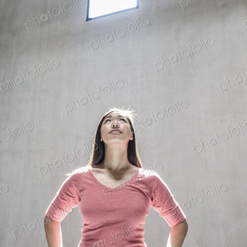 Asian woman standing underneath the light from a window in a new warehouse.