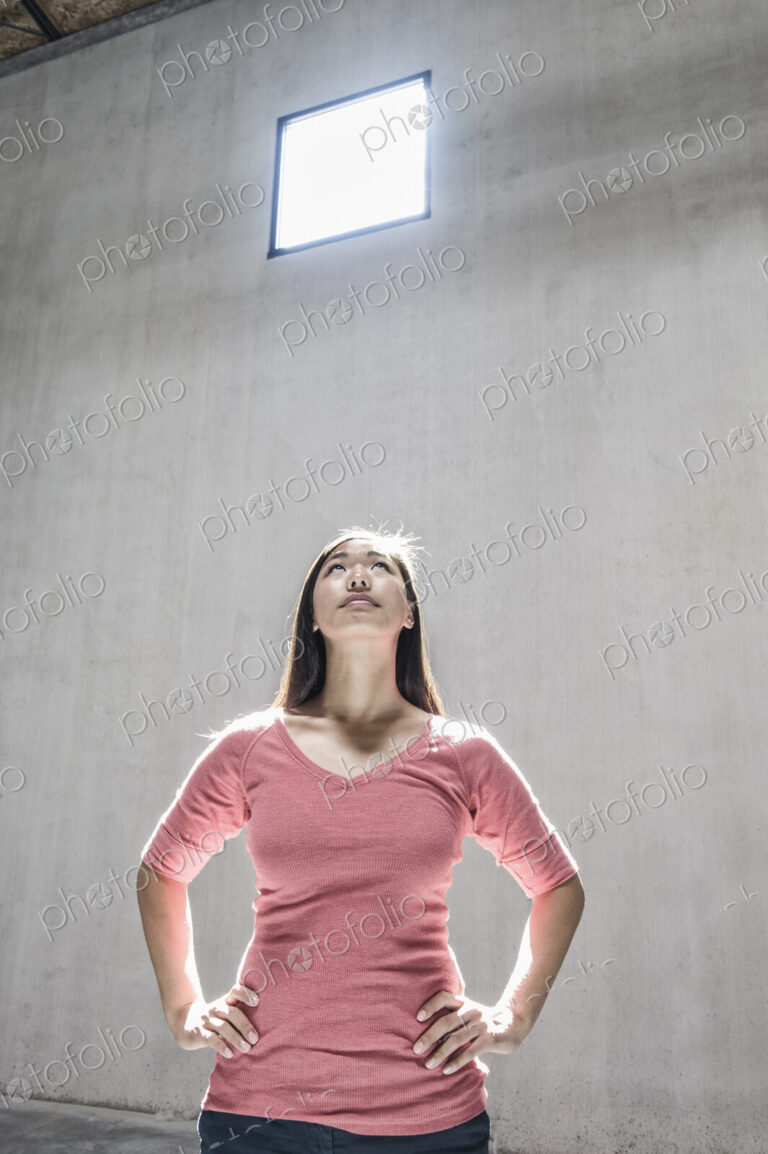 Asian woman standing underneath the light from a window in a new warehouse.