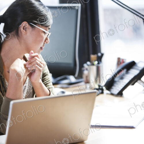 Asian woman working at her desk in a creative office. Asian woman working at her desk in a creative office.