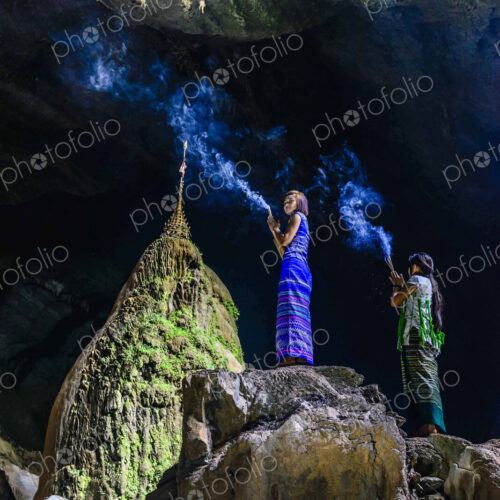 Asian women burning incense on rock formation in cave temple Asian women burning incense on rock formation in cave temple