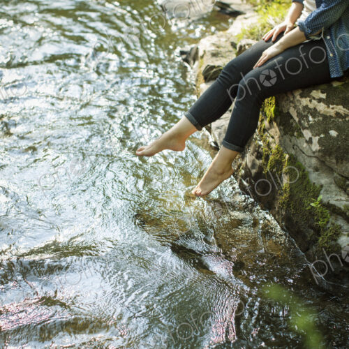 Awoman sitting at the water's edge paddling her feet in the stream. Awoman sitting at the water's edge paddling her feet in the stream.