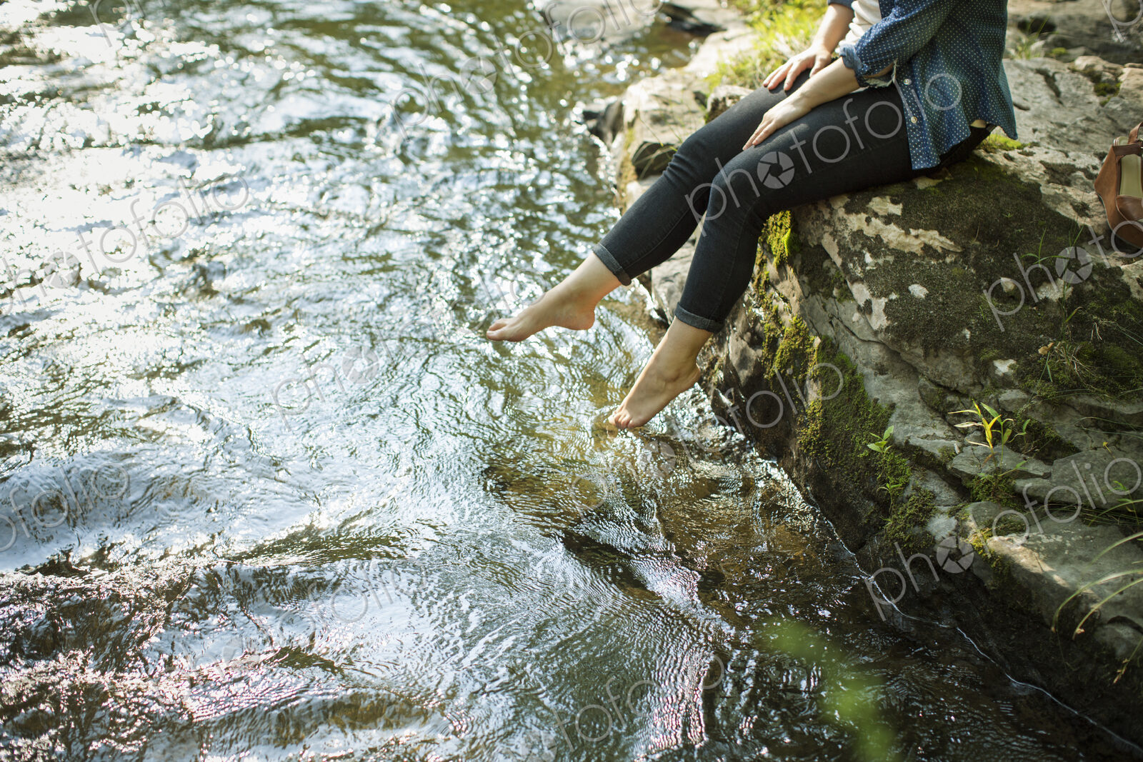 Awoman sitting at the water’s edge paddling her feet in the stream.