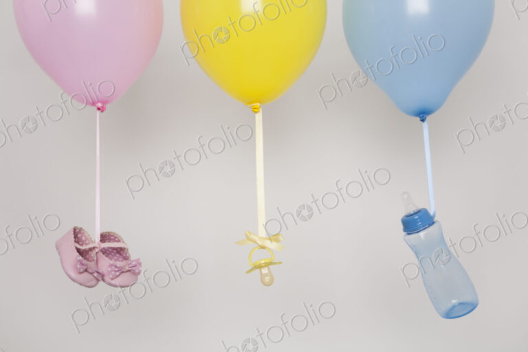 Baby bottles, pacifier and baby shoes tied by ribbon to balloons.