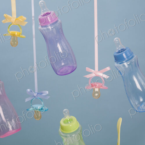 Baby feeding bottles, baby spoons and pacifiers hanging from ribbons.