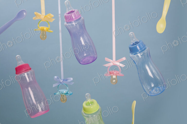 Baby feeding bottles, baby spoons and pacifiers hanging from ribbons.