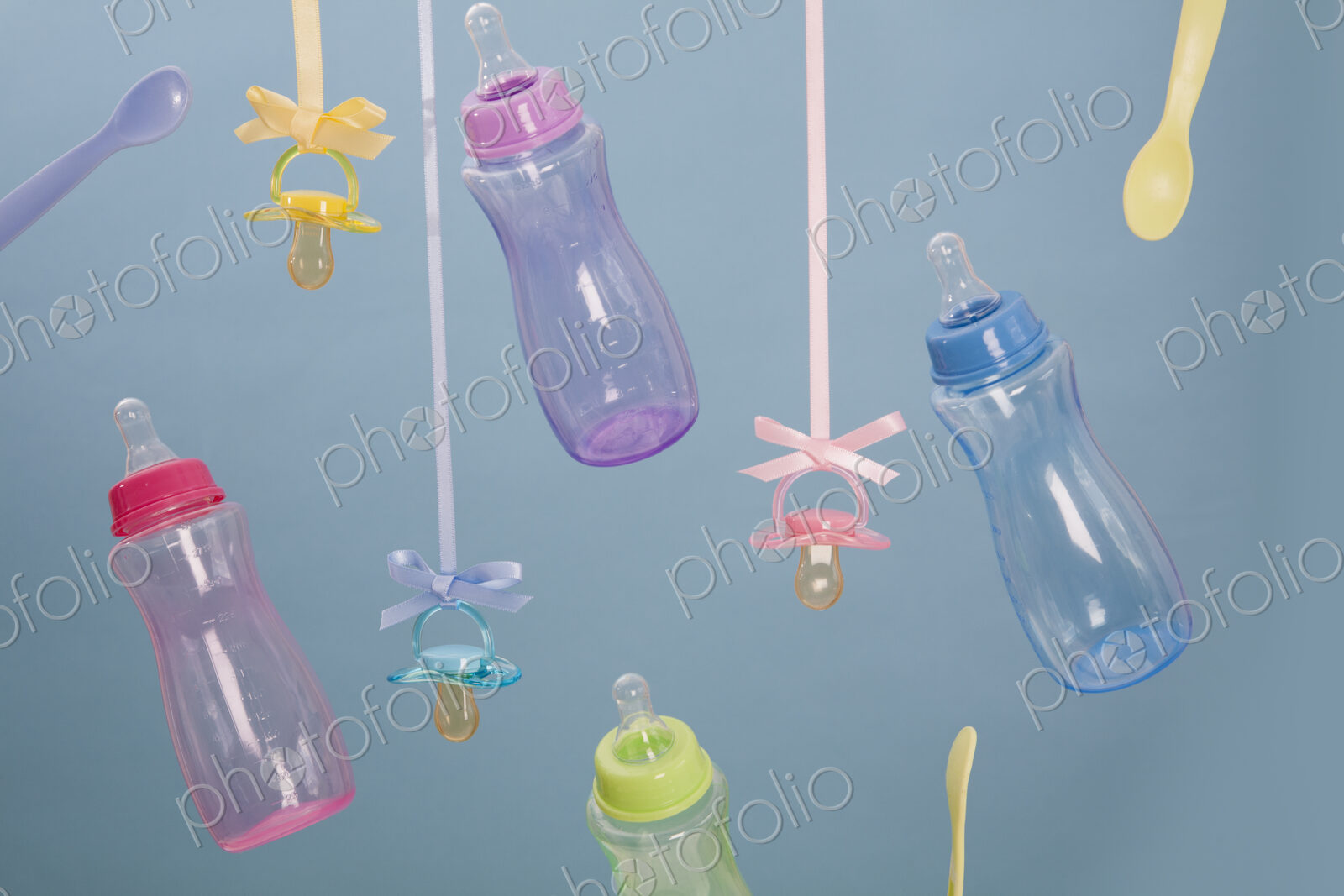 Baby feeding bottles, baby spoons and pacifiers hanging from ribbons.