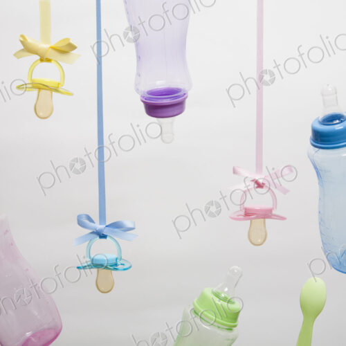 Baby feeding bottles, baby spoons and pacifiers hanging from ribbons.