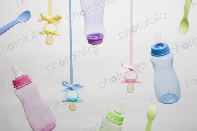 Baby feeding bottles, baby spoons and pacifiers hanging from ribbons.