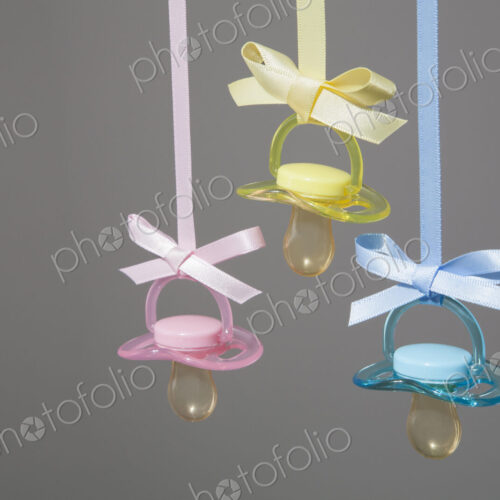 Baby pacifiers hanging from ribbons against a plain background.