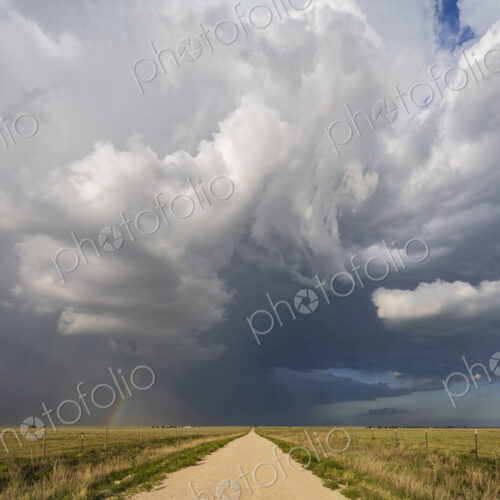 Back Side of a Supercell with a Rainbow above a road reaching the horizon. Back Side of a Supercell with a Rainbow above a road reaching the horizon.