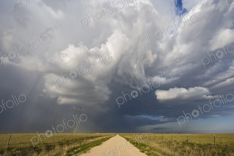 Back Side of a Supercell with a Rainbow above a road reaching the horizon.