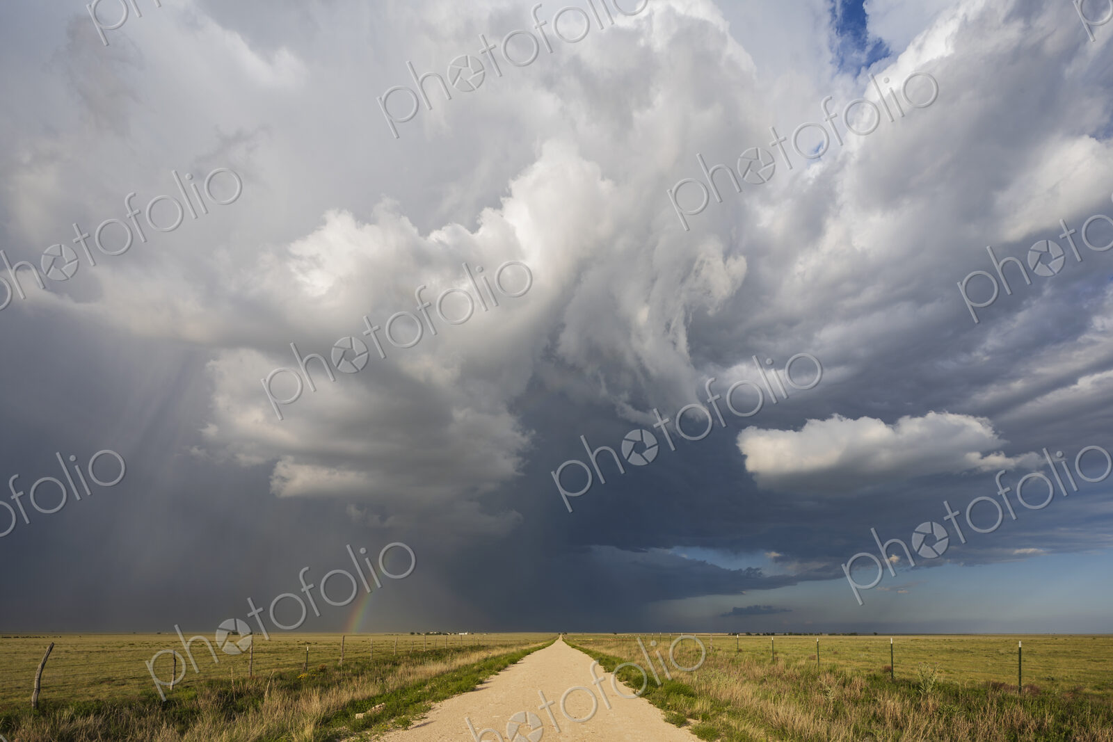 Back Side of a Supercell with a Rainbow above a road reaching the horizon.