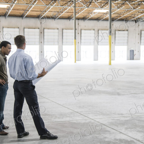 Back man owner of new warehouse and caucasian man architect going over blue print…