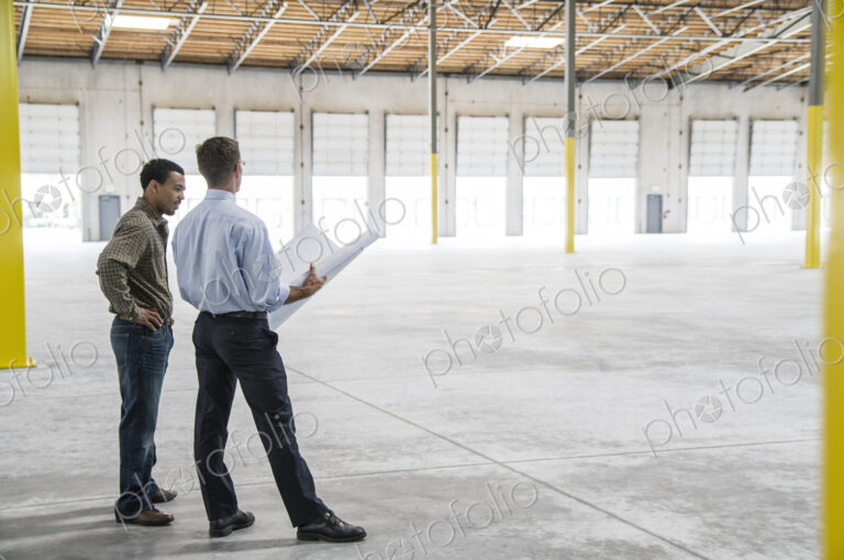 Back man owner of new warehouse and caucasian man architect going over blue print…
