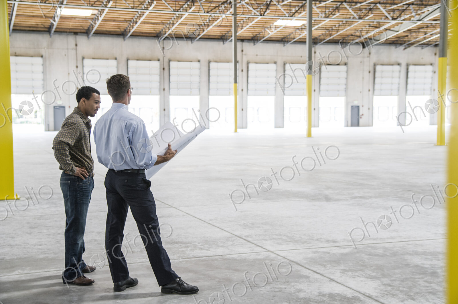 Back man owner of new warehouse and caucasian man architect going over blue print…
