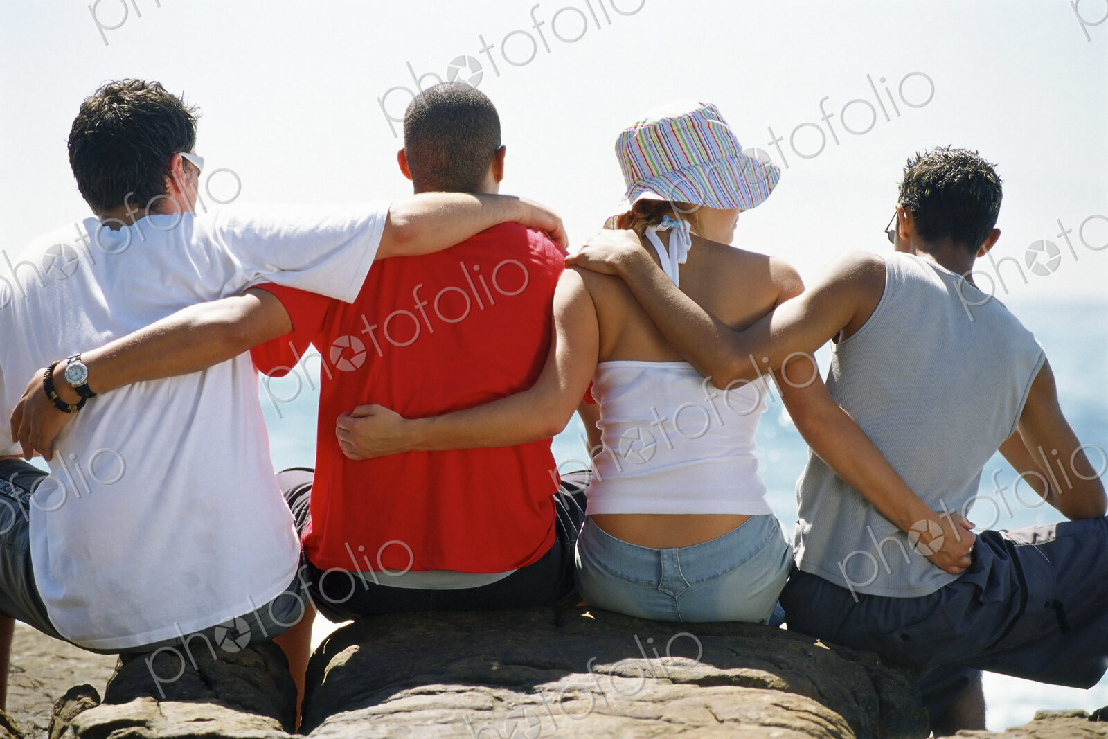 Back view of four friends, with arms around each other, sitting in a row.