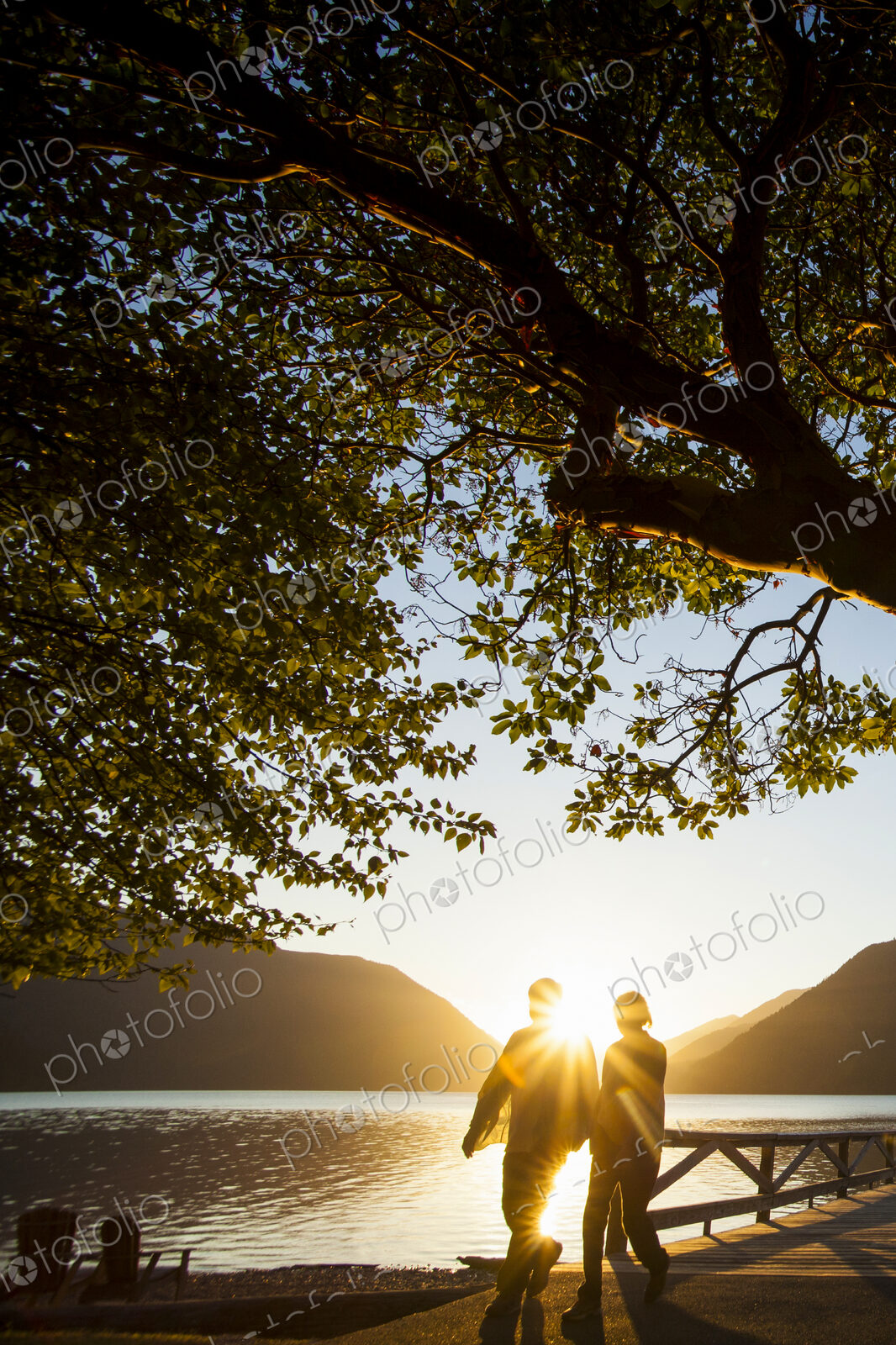 Backlit couple standing by lake Crescent at sunset, Olympic National Park.