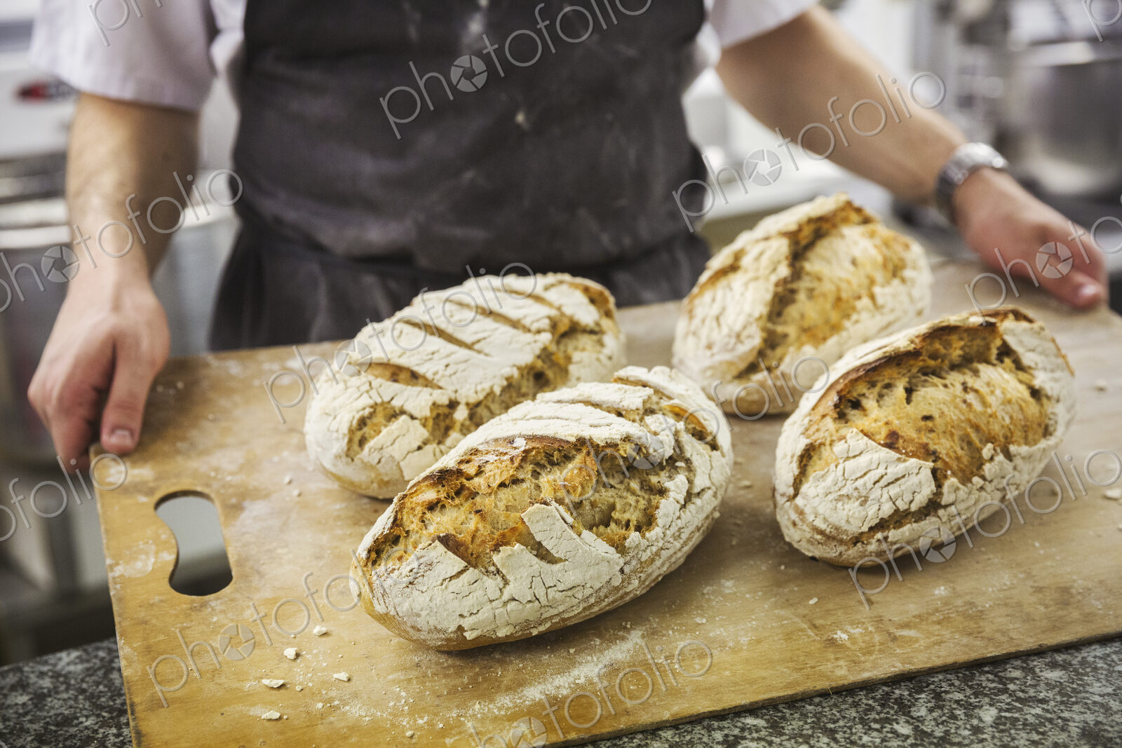 Baker holding tray with freshly baked loaves of bread.