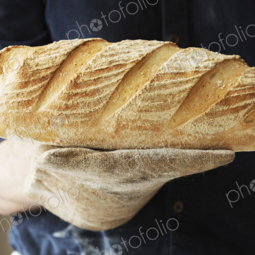 Baker holding two freshly baked loaves of bread.