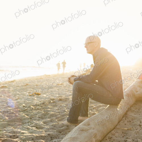 Bald man sitting on a log on a sandy beach. Bald man sitting on a log on a sandy beach.