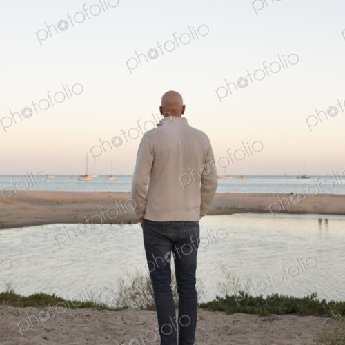 Bald man standing on a sandy beach by the ocean. Bald man standing on a sandy beach by the ocean.