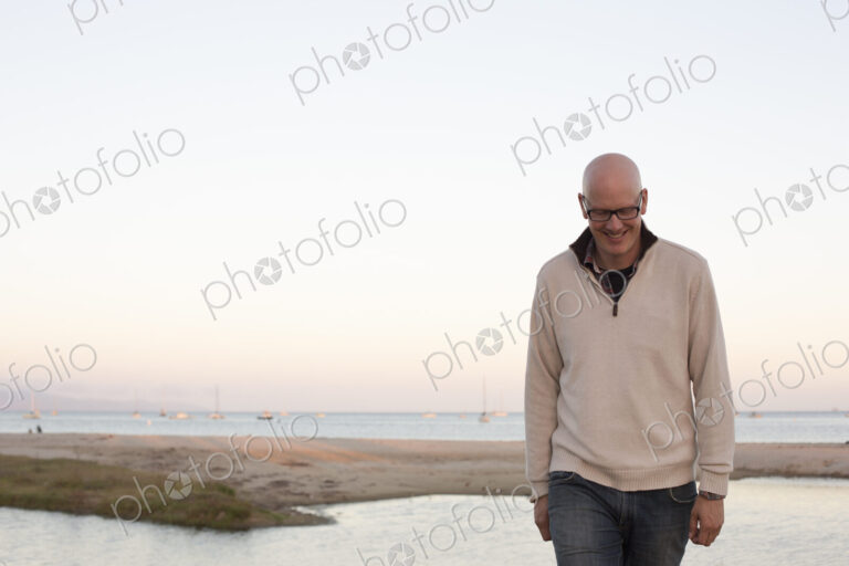 Bald man walking on a sandy beach by the ocean.