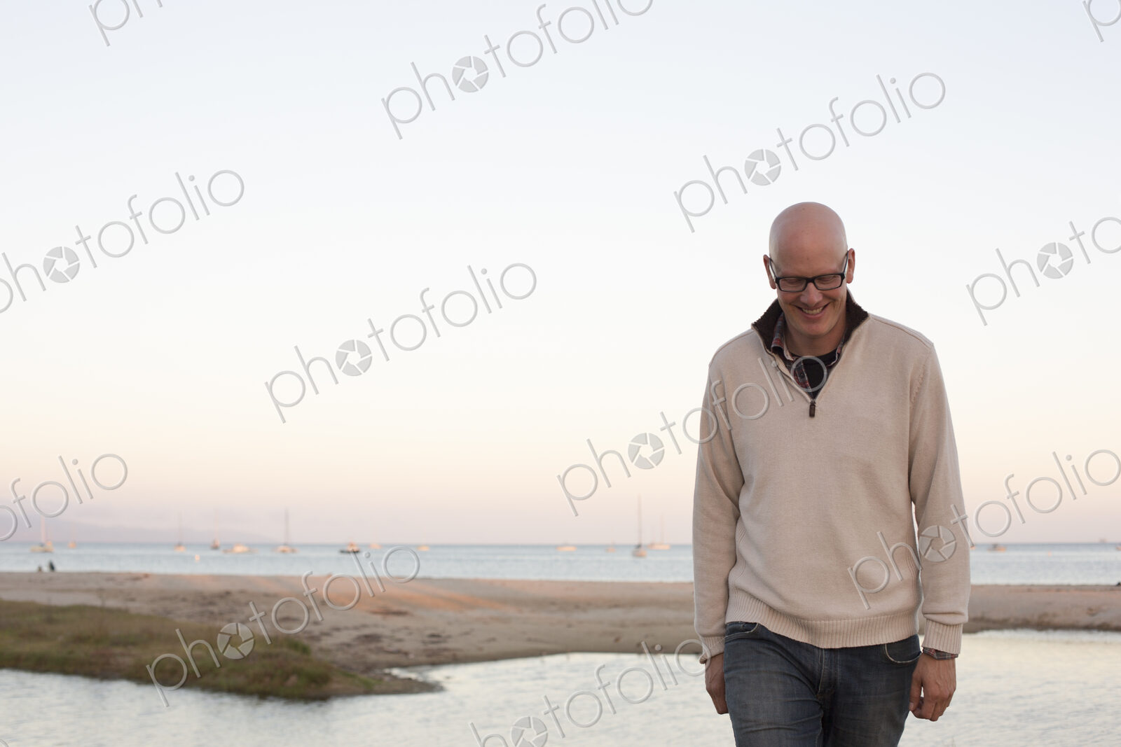 Bald man walking on a sandy beach by the ocean.