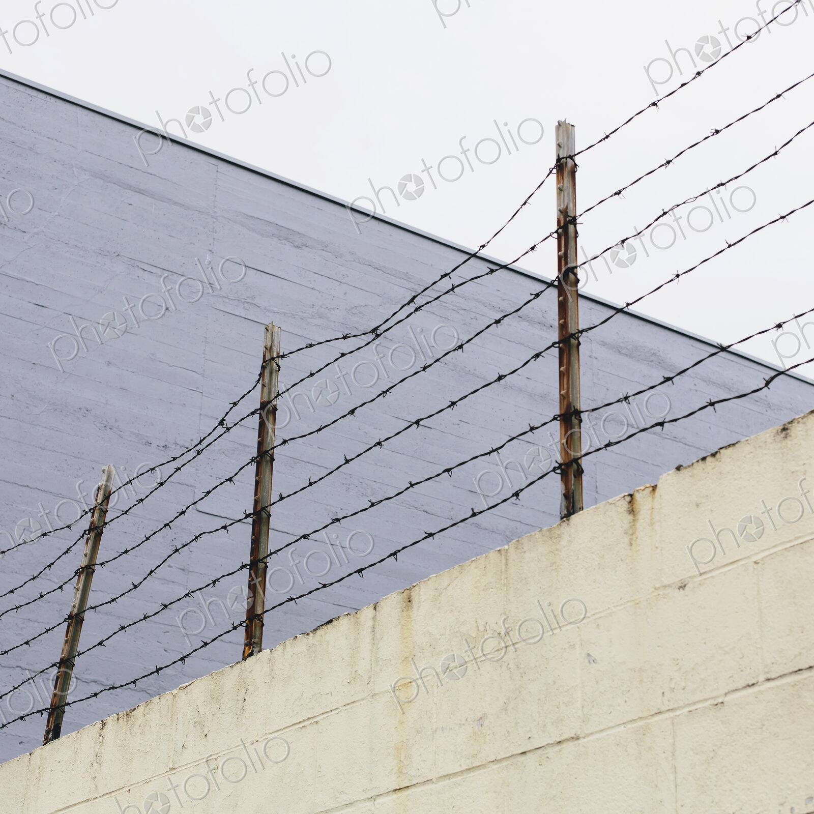 Barbed wire fence at the top of a wall, in a city.