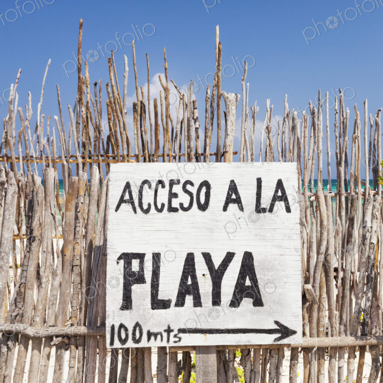 Beach access sign in Spanish,on a fence by the beach