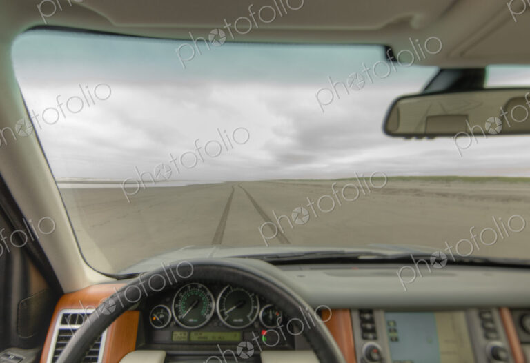 Beach and cliffs seen from driver's seat of a car, with steering wheel in foreground.
