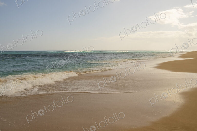 Beach and surf along Oahu's wild North Shore with waves breaking far from the shore.