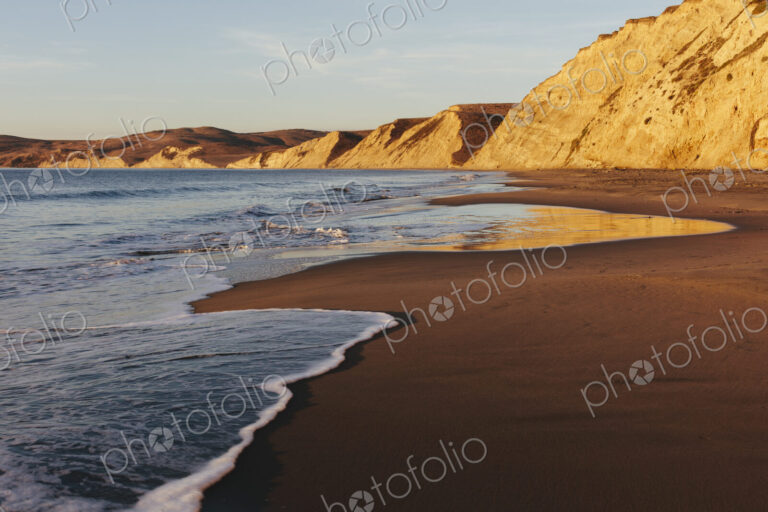 Beach at dawn, with sheer cliffs and rocks.