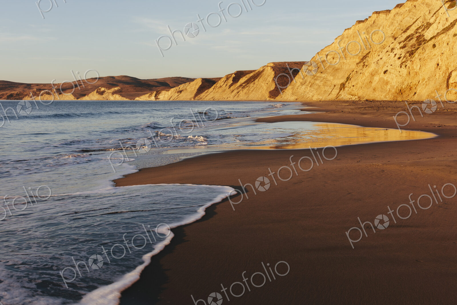 Beach at dawn, with sheer cliffs and rocks.