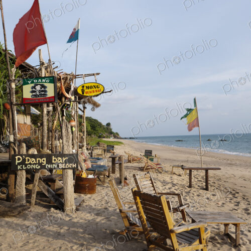 Beach bar and cabins on a sandy beach, with flags and furniture, on the Andaman coast.
